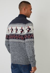 Maglione lavorato a maglia in navy, crema e rosso. Presenta un design festivo con pinguini, fiocchi di neve e un motivo testurizzato su tutto il corpo.