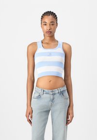 Lys blå og hvite stripete ribbet crop topp med brede stropper; kombinert med lyseblå løst sittende jeans. Enkel logo etikett i midten.
