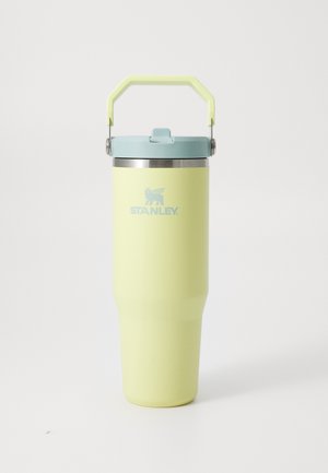 Contenedor para bebida Stanley alto, amarillo pálido aislado, con tapa azul claro y asa plegable sobre fondo blanco.