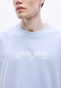 Svetlomodré bavlnené tričko s okrúhlym výstrihom, na ktorom je biely potlačený nápis "calvin klein new york city."