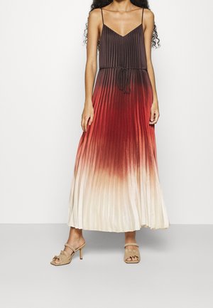 Donna che indossa un abito maxi plissettato con colori sfumati nero, rosso e crema, sottili spalline e sandali beige con tacco.
