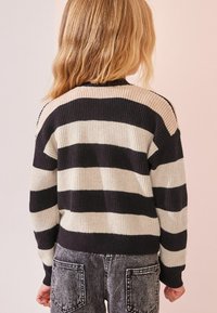 Strickpullover im schwarz-weißen Streifenmuster mit rundem Halsausschnitt; kombiniert mit grauen Jeans mit Gesäßtaschen und strukturierter Oberfläche.