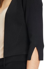 Svart kortärmad cardigan med trekvartslånga ärmar, med utskärningsdetalj vid manschetten och en texturerad stickad tyg.