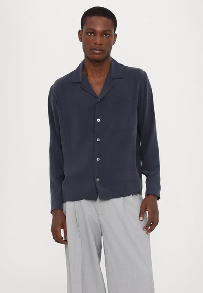 Camisa de botón de color azul marino en tejido ligero con un corte relajado, cuello con muesca, bolsillo en el pecho y botones plateados brillantes.