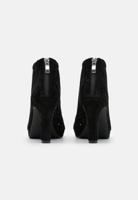 Černé semišové kotníkové boty na vysokém podpatku, s texturovaným zadním panelem a bočními výřezy, a kovovým zipem na zadní straně.