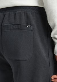 Zwarte sweatpants met een elastische tailleband, een enkele achterzak met een gestikte label en een zachte, gestructureerde stof.