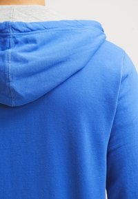 Sudadera azul de textura suave de algodón, con un forro interior gris en la capucha y un corte relajado. Detalle de costura visible en la parte posterior.