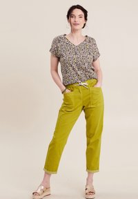 Korte mouw top met een kleurrijk abstract patroon, gecombineerd met groene taps toelopende broek met een elastische tailleband en zakken.