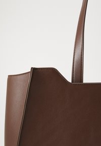 Bruine faux leren schoudertas met een gestructureerde vorm, kenmerkend door een gladde textuur, zichtbare stiksels en een enkele lange hengsel.