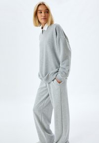 Hellgrauer Sweatshirt mit gesenkten Schultern, einem gerundeten Halsausschnitt und langen Ärmeln, kombiniert mit passenden weiten Sweathosen.