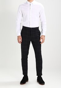 Camicia bianca con bottoni abbinata a pantaloni a quadri neri; forma aderente con texture liscia e scarpe nere. Design semplice e moderno.