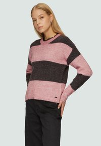 Geribbelde gebreide trui met roze en donkergrijze verticale strepen, ronde halslijn en een klein logo-accent aan de onderrand. Zwarte broek inbegrepen.