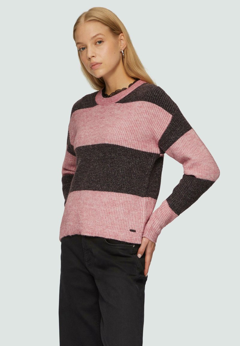 Geribbelde gebreide trui met roze en donkergrijze verticale strepen, ronde halslijn en een klein logo-accent aan de onderrand. Zwarte broek inbegrepen.