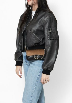 Zwart leren bomberjack met ribbelboorden en schouders, voorzien van zakken en een ritssluiting aan de voorkant, gedragen met een bruine en zwarte handtas.