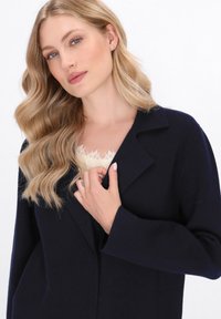Cappotto di lana navy con ampio colletto e maniche lunghe, caratterizzato da uno strato interno testurizzato con bordatura in pizzo e una forma aderente.