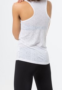 Camiseta ajustada blanca con un patrón texturizado y diseño de espalda de nadador, combinada con leggings negros. Tejido ligero con ligera transparencia.