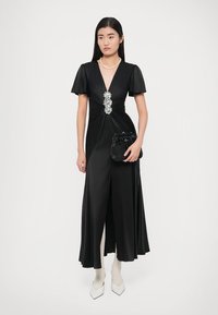 Fekete szatén ruha rövid fodros ujjal, a deréknál drágakő díszítéssel és magas hasítékkal. Fekete kézitáskával és fehér magassarkúval párosítva.