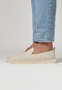 Espadrilles beiges en daim avec une semelle en jute tressé, présentant un design sans lacets et un petit talon.