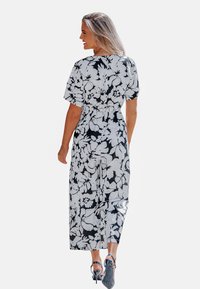 Zwart-witte bloemenmaxi-jurk met korte mouwen, taille accentuerend, en een losse pasvorm, gecombineerd met hoge hakken. Vloeiende stoftextuur.