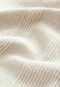 Tissu en tricot beige clair présentant des textures variées, avec des motifs lisses et côtelés, d'apparence douce et légèrement duveteuse.