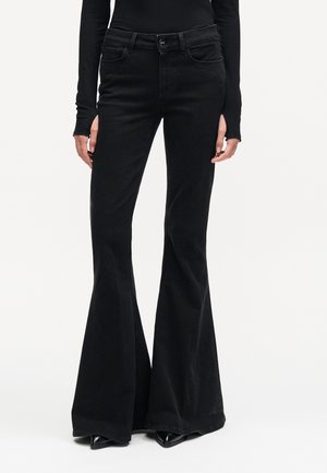 Zwarte high-waisted wijde jeans, gedragen met zwarte puntige schoenen en een lange mouwen zwarte top, getoond van taille tot voeten.