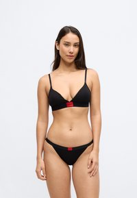 Μαύρο σετ μπικίνι με τριγωνικό μπουστάκι με λεπτές τιράντες και κόκκινη λωρίδα με το λογότυπο, σετ με αντίστοιχο σλιπ χαμηλής μέσης. Λεία υφή.