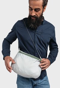 Borsa a tracolla bianca in nylon con zip verde, forma curva e logo impresso. Indossata da una persona con una maglietta scura, tenuta in una mano.