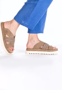 Brown suede sandals with a double strap design and decorative stitching, featuring a textured white sole and a low wedge.