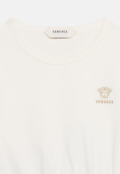 Λευκό T-shirt Versace με στρογγυλή λαιμόκοψη, μικρό χρυσό λογότυπο κεφαλής Μέδουσας και κείμενο Versace στο πάνω αριστερό μέρος του στήθους.