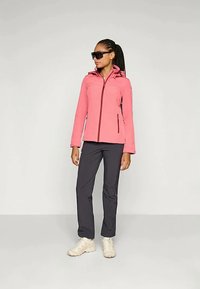 Rosa jakke med lynlås og hætte, parret med mørke bukser og lyse sneakers. Jakken har sidelommer og et tætsiddende design.