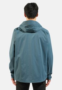 Water-resistant jacket in teal, featuring a hood and long sleeves, with a smooth texture and a slightly loose fit, seen from the back.