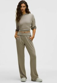 Világos taupe, rövid fazonú kapucnis pulóver hosszú ujjakkal, széles szárú nadrággal párosítva. Puha, rugalmas anyag, oldalsó zsebekkel és sima textúrával.