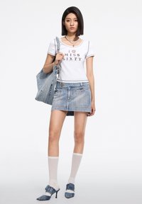 Tricou alb cu imprimeu "ÎMI ESTE DOR DE SIOUX", asortat cu o fustă mini din denim albastru și pantofi cu toc înalt albaștri. Accesoriile includ o geantă din denim și șosete până la genunchi.
