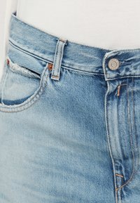 Φωτεινό γαλάζιο τζιν με ψηλή μέση, χαλκομανία κουμπί και κλασικό σχέδιο με πέντε τσέπες. Διαθέτει ελαφριά ξεθώριασμα και διακοσμητικές ραφές.