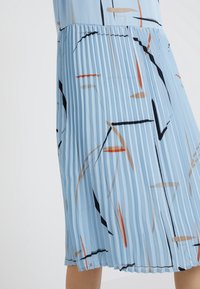 Abito plissettato azzurro chiaro con motivi astratti in nero, arancione e beige. Texture liscia e lunghezza fino al polpaccio, con vita arricciata.