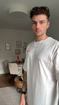 Hvid bomulds T-shirt med rød tekst, korte ærmer og en afslappet pasform, båret med en sølv kæde halskæde. Baggrunden viser et spisestue.