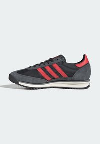 Zapatilla deportiva de ante gris con parte superior de tela negra, tres franjas rojas y entresuela blanca. Tacón texturizado y suela de goma.