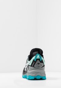 Baskets de course noires et vert menthe avec une tige texturée, des accents réfléchissants et une semelle robuste présentant des détails en teal et un logo de montagne.