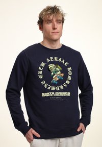 Sudadera de color azul marino con un gráfico redondo que presenta a un esqueleto de dibujos animados en un traje de astronauta haciendo skate. Incluye el texto "Santa Monica Space Cruisers".