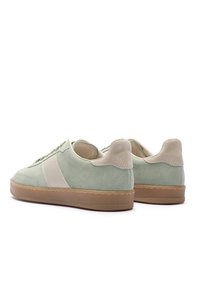 Para jasnozielonych zamszowych trampek z beżowymi akcentami i gumowymi podeszwami w kolorze gumy, widocznych od tyłu na białym tle.