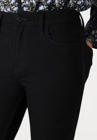 Black denim pants featuring a slim fit, front pockets, and a button closure. The fabric has a smooth texture and minimal stitching details.