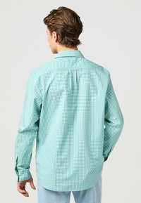 Camisa de manga larga en un patrón a cuadros verde claro y blanco. Incluye un collar clásico y puños abotonados. Tejido ligero.