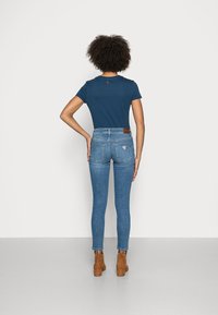 Modrá tričko s krátkým rukávem spárované s vysokými, slim-fit modrými džíny. Výrazná hnědá kožená nášivka značky na zadním pasu, ladící hnědé boty na podpatku.