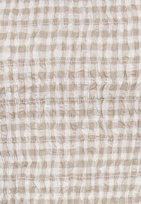 Tecido plissado em padrão de quadrados bege e branco, apresentando pregas horizontais texturizadas e uma aparência ligeiramente transparente.