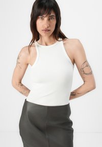 Hvit ribbet tanktop med høy hals, kombinert med en mørk lærskjørt. Tatoveringer synlige på armen, med et glatt, tettsittende design.