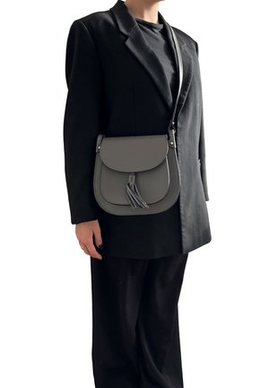 Persona che indossa un blazer nero e pantaloni, con una borsa a tracolla grigia con un dettaglio a frange sulla spalla.