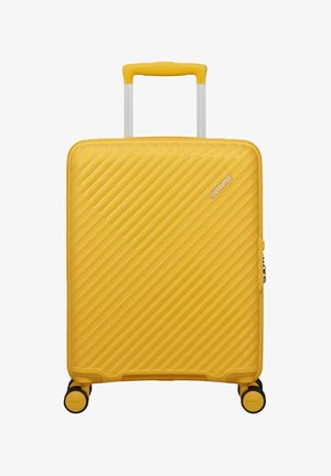 Valigia rigida gialla con scanalature diagonali, manico estendibile, quattro ruote e logo American Tourister sulla parte anteriore.
