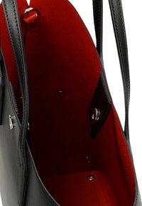 Černá kožená taška přes rameno s červeným interiérem. Má dlouhé popruhy, patentní uzávěr a hladký povrch. Interiér obsahuje kovové doplňky a kapsy.