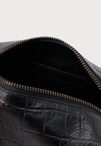 Sort taske i krokodillepræget læder med en metallisk lynlås og en glat indvendig foring. Designet har en rektangulær form.