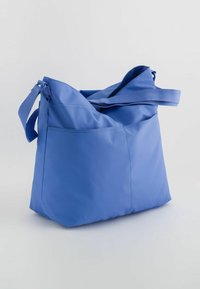 Blue fabric shoulder bag with a smooth texture, featuring a wide opening and an external pocket. The strap is adjustable for convenience.